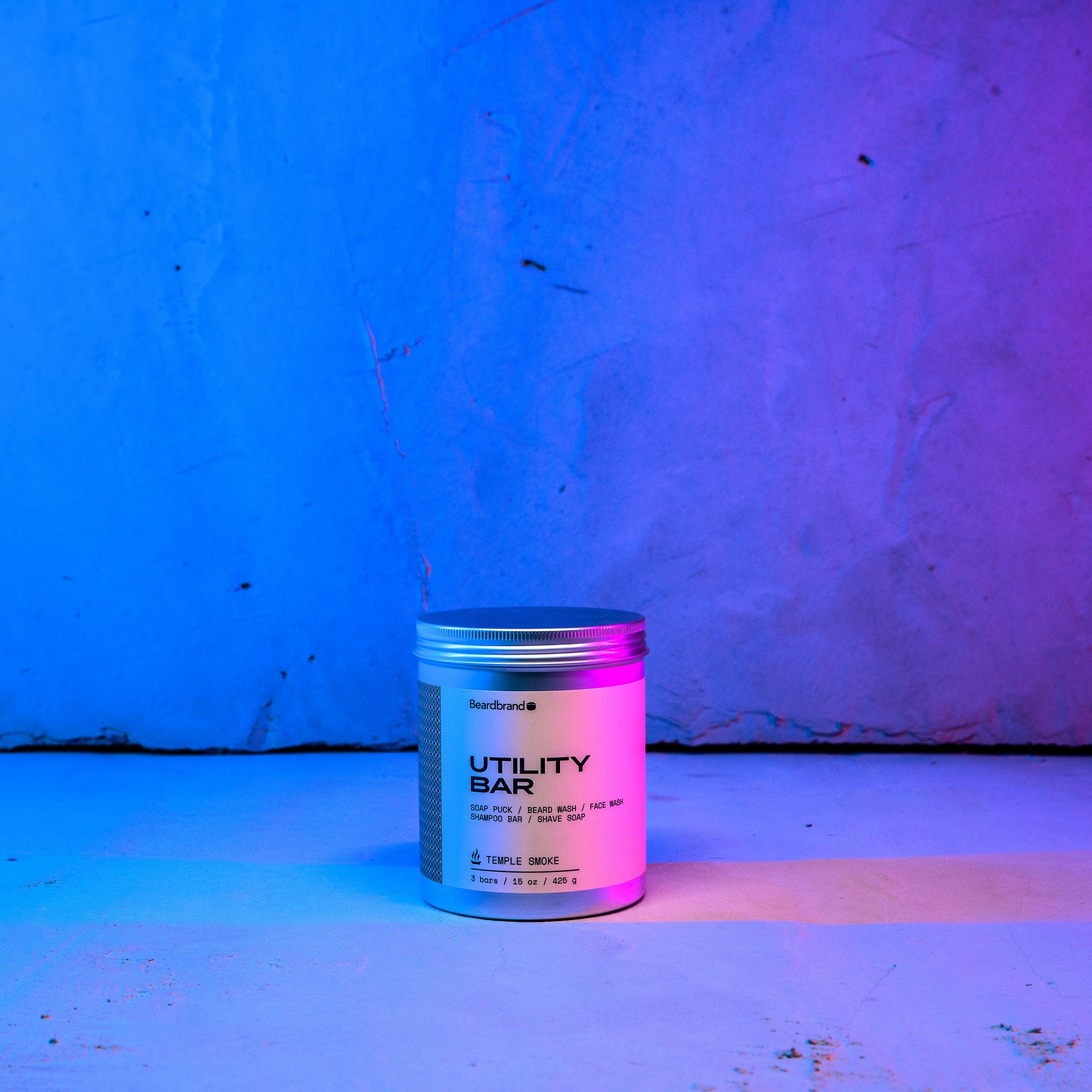 Beardbrand's Utility Bar 3-pack set on a concrete backdrop highlighted in blue and pink lighting with the label facing forward.