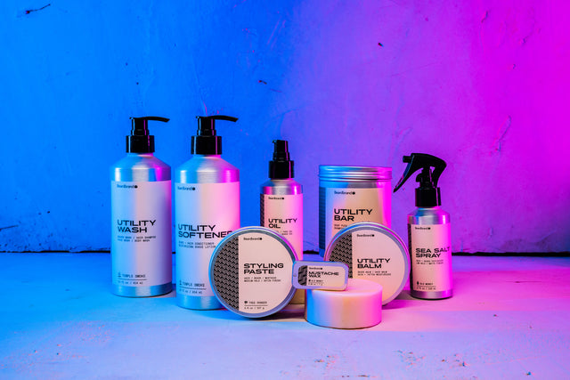 Beardbrand products in aluminum packaging arranged together against a concrete backdrop lit up in neon blue and pink.