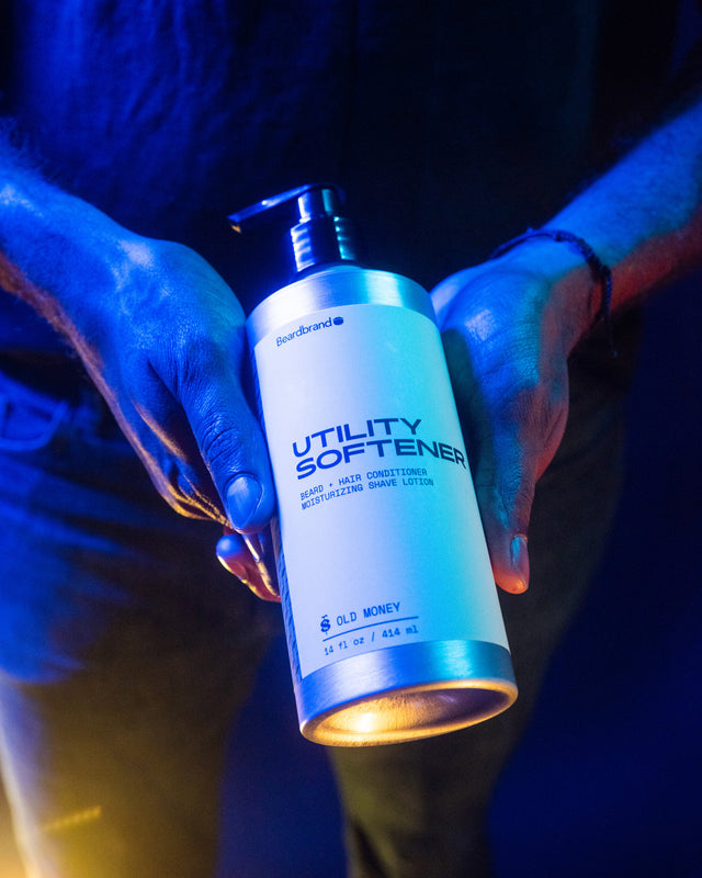 A person holding a bottle of Beardbrand Utility Softener in their hands highlighted in vibrant lighting.