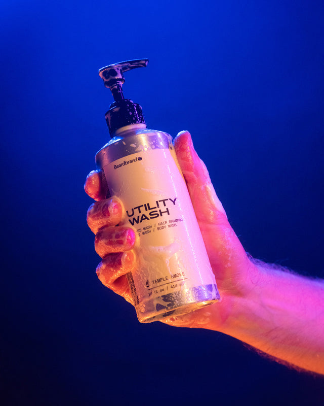 A person in vibrant lighting holding a sudsed up Beardbrand Utility Wash bottle.