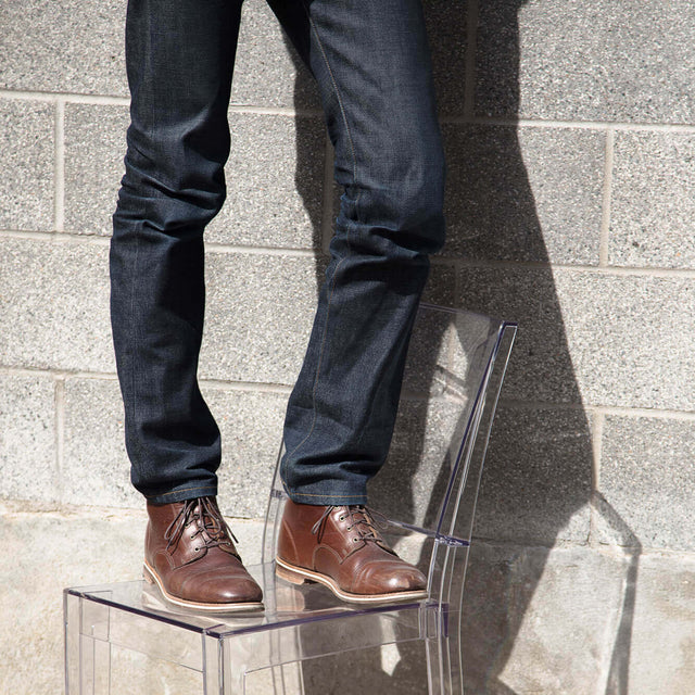 A person in jeans and heritage boots standing on a clear acrylic chair.