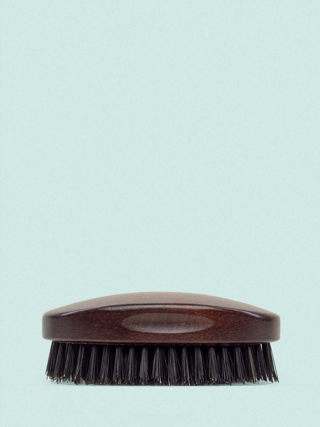 A Beardbrand 100% Boar’s Hair Oval Brush side view against a striking blue backdrop.