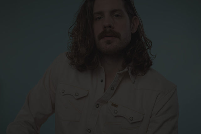 Mike facing forward wearing a cream colored pearl snap shirt against a turquoise background