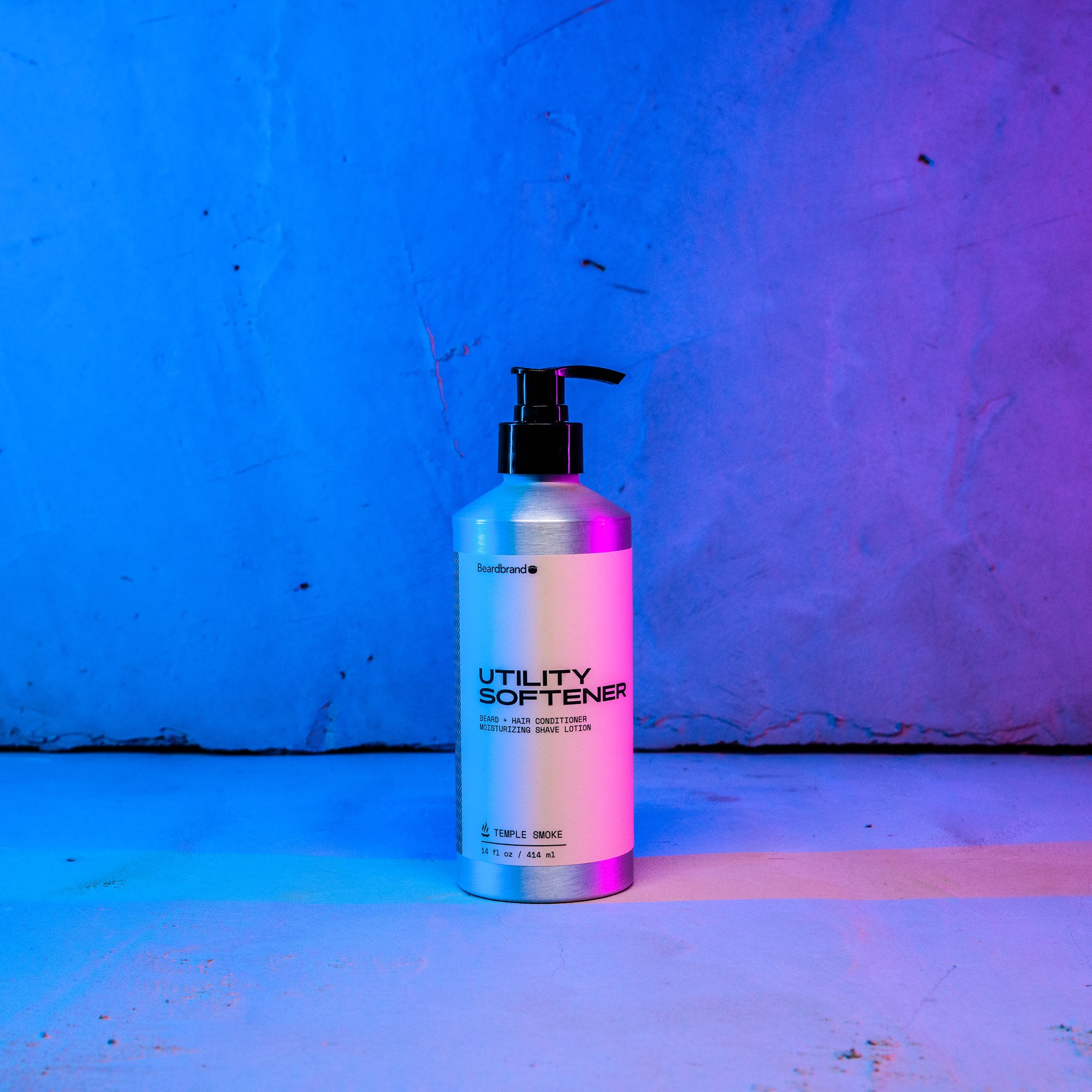 Beardbrand's Utility Softener set on a concrete backdrop highlighted in blue and pink lighting with the label facing forward.